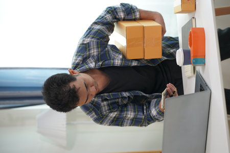 Young Asian man packs parcels for customers Electronic commerce, online shopping, SME business concept. A man holds a package box preparing to send it to a customer.の写真素材