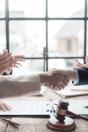 Close-up of a male lawyer making a deal and shaking hands with a male client at the table in his office. Office with judge's gavel and scale on table. Lawの写真素材