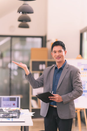 Young Asian businessman smiling while working with laptop computer and financial documents at office Concept of living a successful business lifeの写真素材
