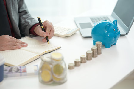A person who puts coins in a piggy bank to save money and invest for future growth with a pile of coins in front of him planning financial cost management.の写真素材