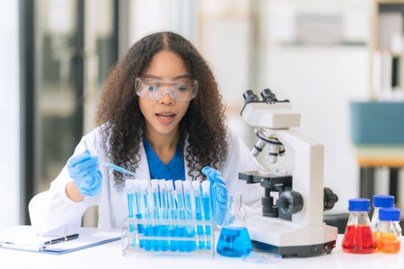 Beautiful African female doctor sitting at table in science lab with test flasks Colorful glass bottles filled with various liquids on a wooden table in a laboratoryの写真素材