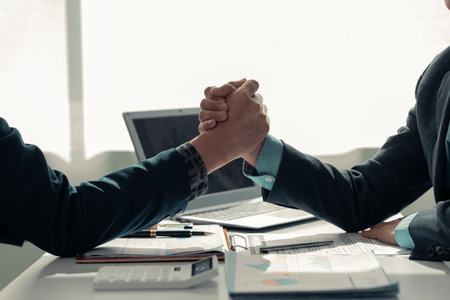 shaking hands showing collaboration and financial success with graphs, data charts displayed on a table with a laptop, close-up imageの写真素材