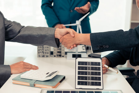 Close-up of a handshake between a real estate agent and a businessman with a small house plan in the background. Real estate, housing, transactions, contract concepts.の写真素材