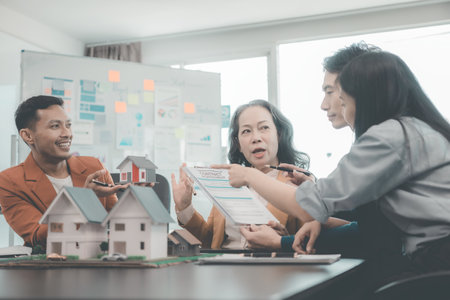 Real estate business meeting with wooden house models on documents, laptops and people discussing construction of single family homes, townhomes for housing projects.の写真素材