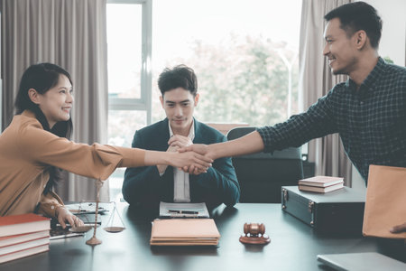 Lawyer shaking hands with client in her office representing legal services and signing agreement with hammer and scales of justice in foregroundの写真素材