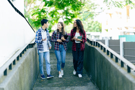 Diverse young university students working outdoors using laptops and tablets together discussing learning concepts.の写真素材