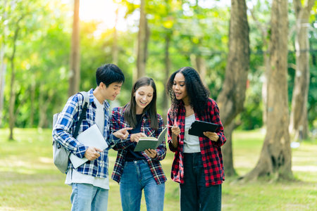Diverse young university students working outdoors using laptops and tablets together discussing technology learning concepts.の写真素材