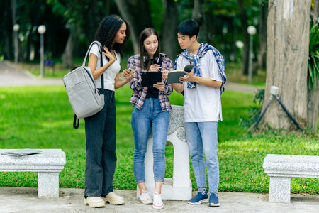 Diverse young university students working outdoors using laptops and tablets together discussing technology learning concepts.の写真素材