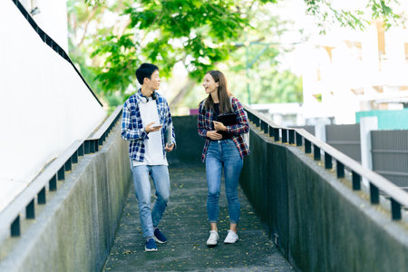 Diverse young university students working outdoors using laptops and tablets together discussing technology learning concepts.の写真素材