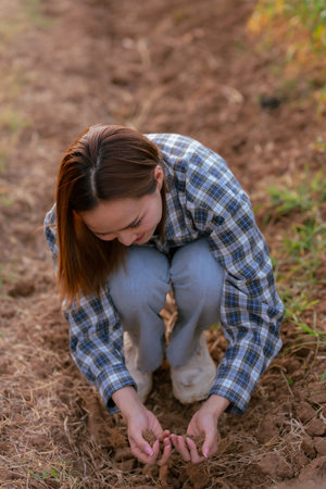Asian female farmer checks soil in hand while working on farm to grow quality cropsの写真素材
