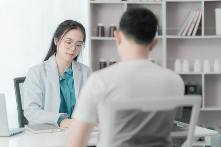 Young Asian man explains symptoms to psychologist while female doctor takes notes at clinicの写真素材