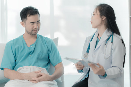 Young Asian man explains symptoms to psychologist while female doctor takes notes at clinic.