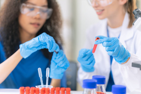 Two female scientists examine liquids in test tubes in a modern laboratory, handling chemicals and experimental materials with precision while wearing special protective suits.の写真素材