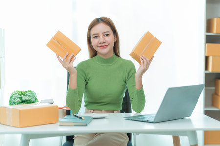 Pretty Asian woman smiling reading parcel while checking customer address on phone. Online...
