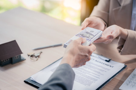 Real estate agent with documents to buy new house of house plan and keys on table. At table with...