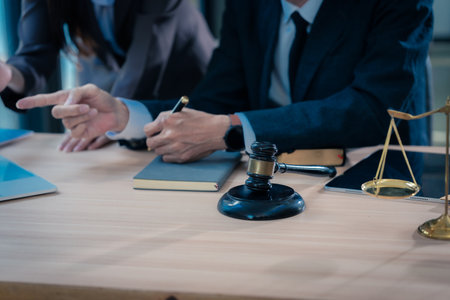 Law office with legal books and scales on table. Legal consultation: lawyer and client reviewing documents together. Representing trusts and legal proceedings. Close-up.の写真素材