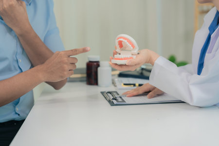Female dentist explains dental problems, gives advice or consults Asian male patient about oral care...