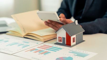 Real estate agent using laptop at desk with miniature model of house, representing real estate investment, buying a house, close up.の写真素材