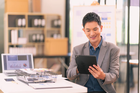 Asian businessman holding digital tablet, standing alone in workspace, looking at camera, using modern web technology for business project management.の写真素材