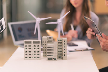 Team of engineers meeting with wind turbines with house models and blueprints placed on tables with...
