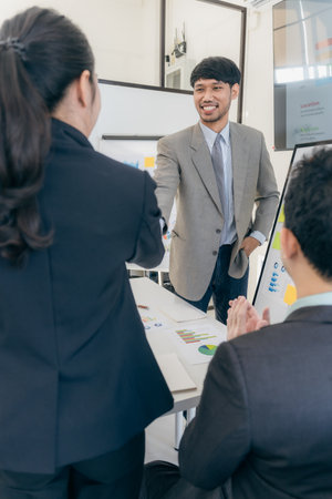 Business team in office and shaking hands after signing contract. Business colleagues clasp hands around desk with laptop and data chart in office.の写真素材