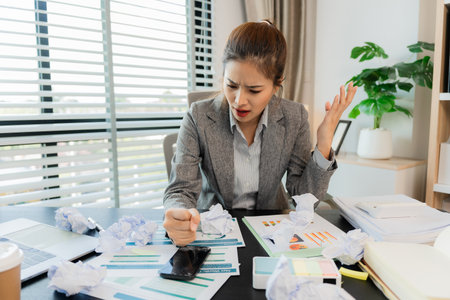 Asian businesswoman stressed holding crumpled paper while working with laptop and documents in office with financial documents and laptop computer. Having problems with work, feeliの写真素材