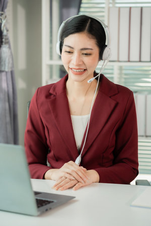 Young Asian woman working as a customer service representative on the phone in an office with a microphone and headset in a customer contact center office. Vertical photo.の写真素材