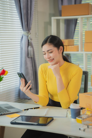 Woman working at home office using laptop and mobile phone. Preparing products for packaging in the background. Concept of SME entrepreneur or freelancer. Vertical image.の写真素材