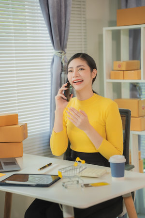 Woman working at home office using laptop and mobile phone. Preparing products for packaging in the background. Concept of SME entrepreneur or freelancer. Vertical image.の写真素材