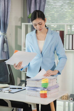 A woman is working with documents on her desk and files. Organizing documents, reviewing financial information. She is reviewing important documents while holding a stack of documeの写真素材