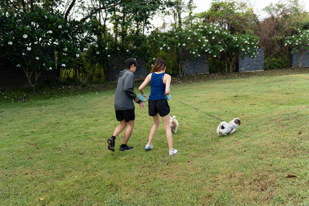 Asian couple walking with their dog in the park in the morning. Friendly pets, a healthy morning...