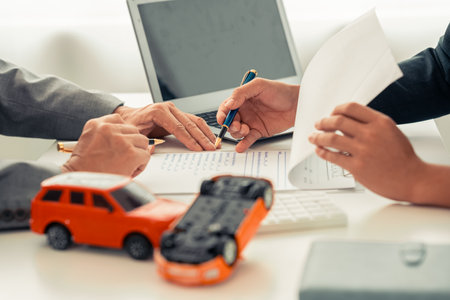 Insurance agent's hand protecting red toy car on table. Planning to manage transportation finance cost. Car insurance business concept.の写真素材