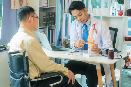 Senior man consults with doctor about joint pain and mobility problems in clinic. Asian male doctor and patient talking in hospital office. Healthcare services.の写真素材