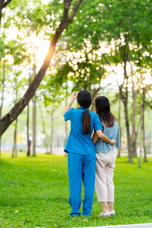 Asian female doctor takes care of elderly female patient in the park, helps the patient walk and exercises her legs and knees in the park.の写真素材