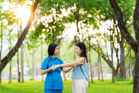 Asian female doctor takes care of elderly female patient in the park, helps the patient walk and exercises her legs and knees in the park.の写真素材