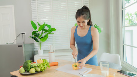 Happy Asian woman enjoys a bowl of fresh salad after a home workout. Enjoying a nutritious meal in a modern kitchen.の写真素材