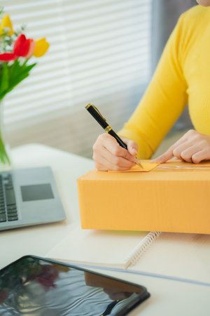 SME supply chain concept, procurement, Asian female entrepreneur taking notes while working on laptop, customer handling orders in small business store.の写真素材