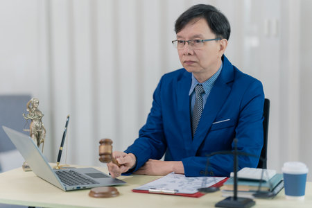 A lawyer or accountant working with a laptop at his desk, reviewing case files in a sharp suit, is...