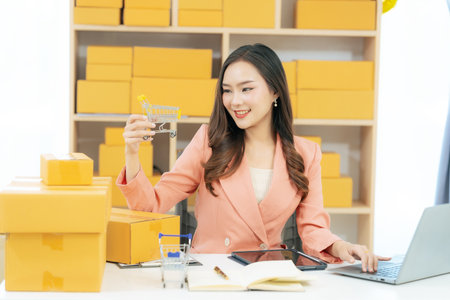 Young Asian woman working from home with laptop computer and parcel box. Online shopping and delivery concept. SME business.の写真素材