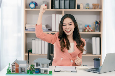 Excited young Asian real estate agent sells her house for investment and offers business and finance presentations.の写真素材
