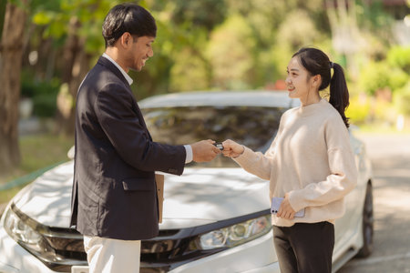 Young couple with car dealer in showroomasian couple holding keys to new car. man and woman standing near the carの写真素材