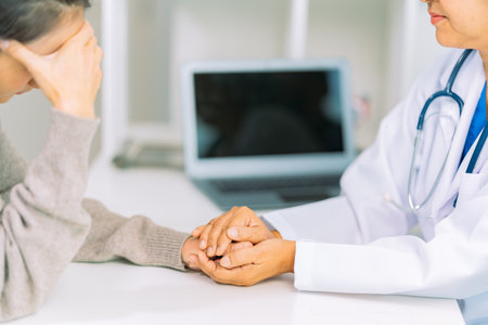 Elderly female doctor and female patient are discussing something while sitting on hospital bed. Medical consultation concept.の写真素材