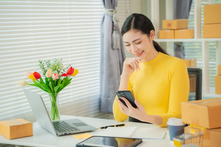 Portrait of young Asian woman using mobile phone, online shopping concept for SME entrepreneurs or freelancers, young small business entrepreneurs working with smartphone at home.の写真素材