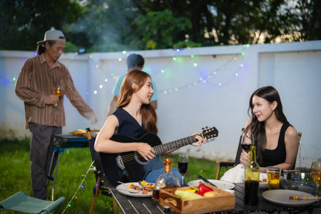 A group of multiracial friends are having a backyard dinner party, clinking beers or sharing drinks...