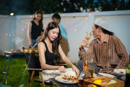 A group of multiracial friends are having a backyard dinner party, clinking beers or sharing drinks. Young people are having fun together and clinking beers whileの写真素材