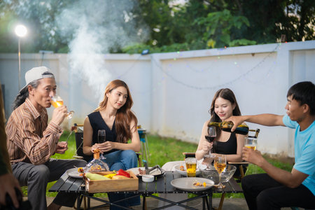 A group of multiracial friends are having a backyard dinner party, clinking beers or sharing drinks during happy hour. Young people are having fun together and clinking beers whileの写真素材
