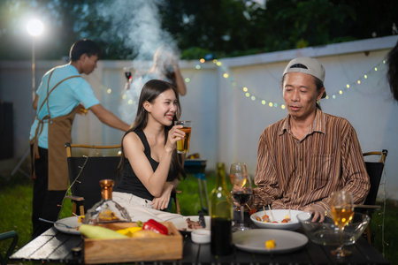 A group of multiracial friends are having a backyard dinner party, clinking beers or sharing drinks during happy hour. Young people are having fun together and clinking beers whileの写真素材