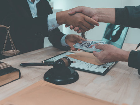 Law Firm, Agreements and Partnerships Two professionals in suits shake hands, a gavel strikes documents and the scales of justice lie on the table in front of them.の写真素材