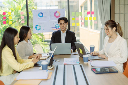 Group of Asian business people presenting data to colleagues in conference room. Business people in suits holding pens pointing at graph documents on table to present company data.の写真素材