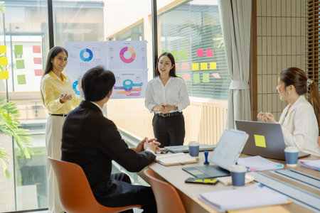 Group of Asian business people presenting data to colleagues in conference room. Business people in suits holding pens pointing at graph documents on table to present company data.の写真素材